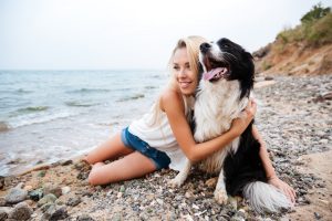 Smiling charming young woman hugging her dog on the beach